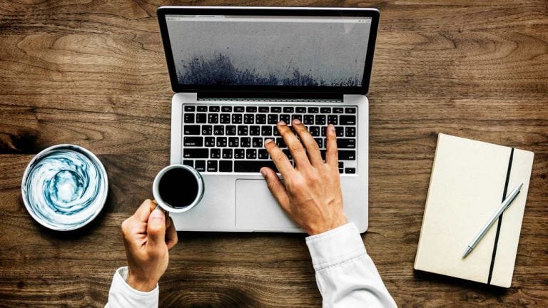 Person typing on laptop with coffee cup.