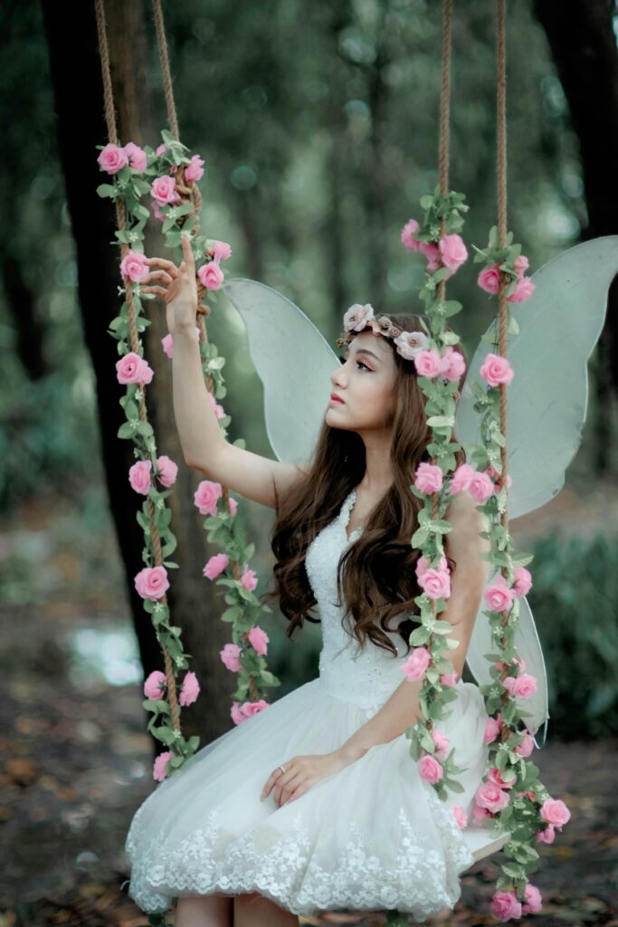Fairy-like woman on floral swing outdoors.