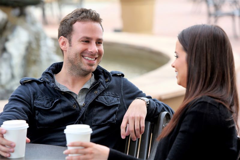 Man and woman chatting over coffee outdoors.