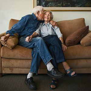 Elderly couple sitting and embracing on couch.