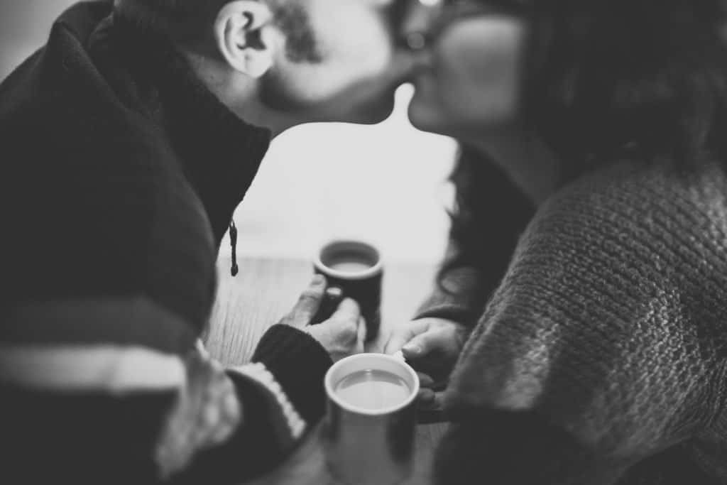 Couple kissing over coffee cups, black-and-white.