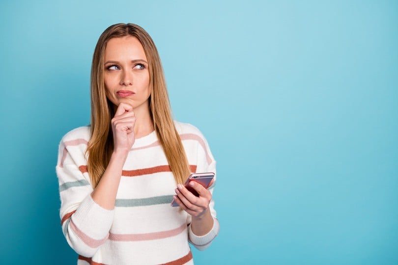 Woman pondering while holding a smartphone.