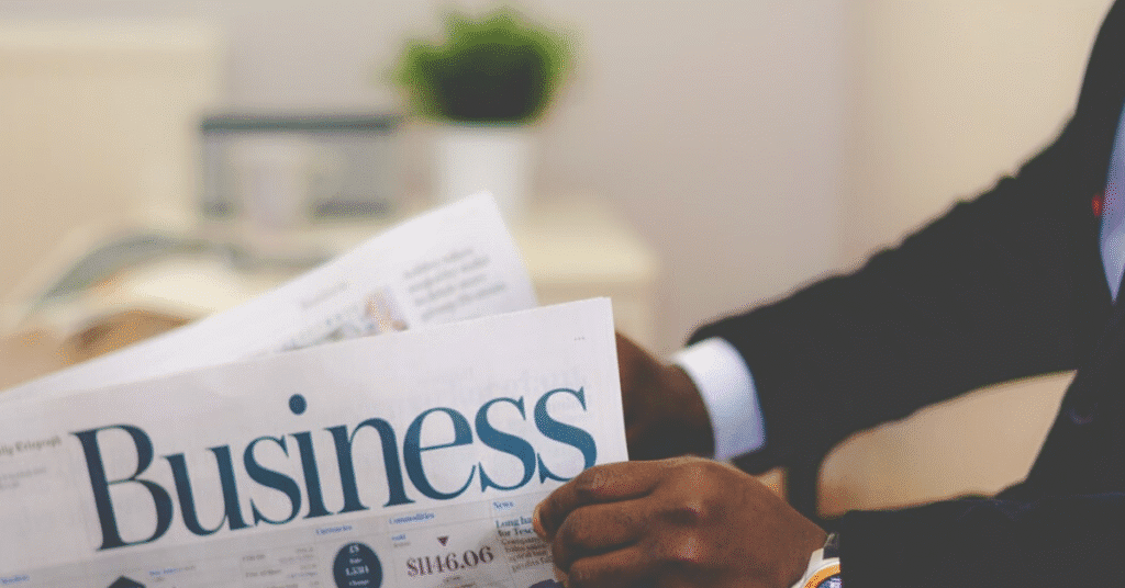 Man reading a business newspaper, plant nearby.