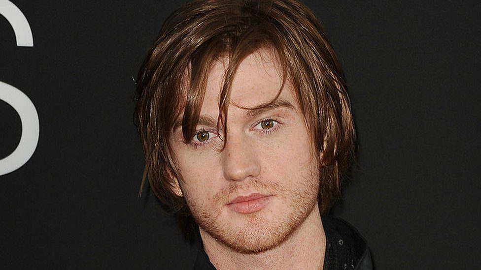 Man with medium-length brown hair, black background.